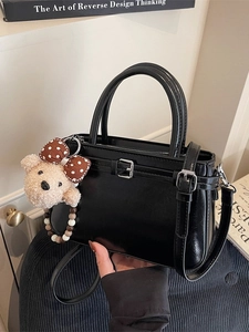 Minimalistische schwarze glänzende Handtasche mit Teddybär-Anhänger und Gurt