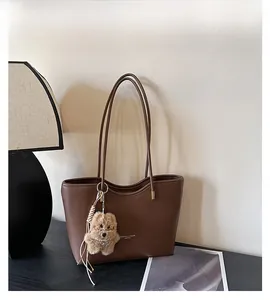 Detail of dark brown leather tote bag with plush bear charm and tassel on wooden table