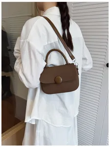 Detail view of dark brown textured crossbody bag with decorative round buckle on a model