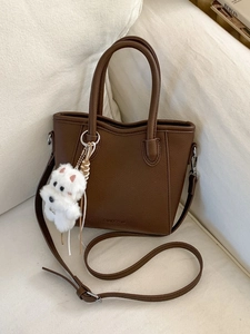 Brown lychee leather bucket bag with top handles and a white plush puppy charm pendant