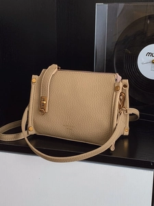 Schicke beige quadratische Umhängetasche aus Leder mit goldenen Details auf Holztisch