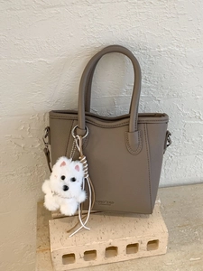 Minimalist taupe bucket handbag with litchi grain texture and plush puppy charm decor