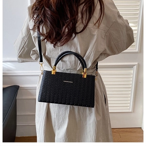 Detail of black woven shoulder bag with golden metal hardware and curved handle