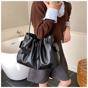 Detail of black drawstring bucket bag with star pendant and side flap pocket