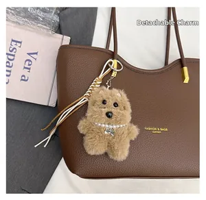 Close-up of plush dog charm with pearl collar on a brown leather tote bag