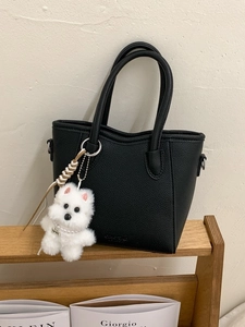 Minimalist black lychee texture bucket bag with a cute white puppy pendant on a wooden stand