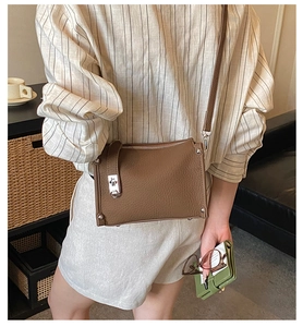 Detail of a brown lychee pattern leather crossbody bag with silver buckle and rivets