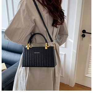 Close-up of black woven texture PU leather handbag with gold metal hardware and strap