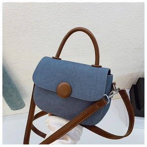 Close-up of blue denim texture handbag featuring a brown round decorative buckle detail