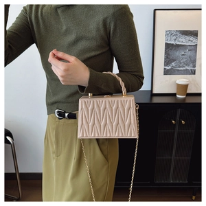 Borsa a scatola trapuntata beige con catena e manico mostrata in una scena lifestyle retrò