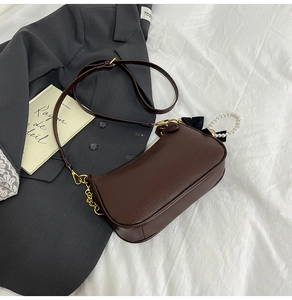 Dettaglio della borsa baguette marrone scuro in pelle martellata con catena di perle