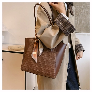 Detail of dark brown tote bag featuring woven texture and silk scarf on handle