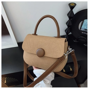 Close-up of beige woven canvas handbag with dark brown leather trim and retro round buckle