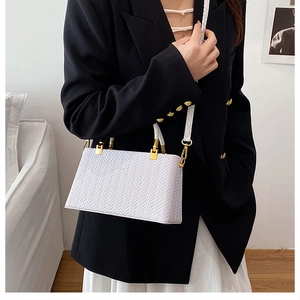 Close-up of white woven handbag with gold hardware and patterned wide strap