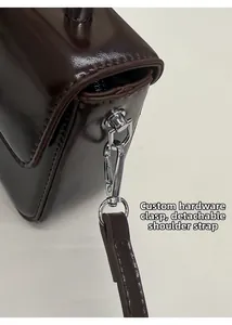 Detail der abnehmbaren Trageriemen mit silbernem D-Ring an der dunkelbraunen Lackledertasche