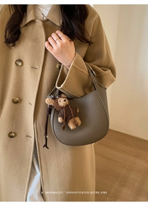 Detail of taupe litchi grain hobo bag with teddy bear charm on wool coat model