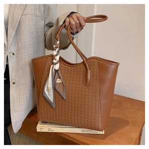 Close-up of brown woven tote bag with smooth leather handles and decorative silk scarf