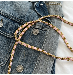 Détail de la bandoulière en cuir rose tressé avec chaîne dorée sur du denim