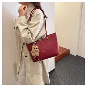 Detail of burgundy lychee grain leather tote bag with gold logo and bear charm