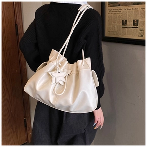 Detail view of a cream drawstring bucket bag with star charm and ruched faux leather texture