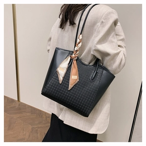 Detail of black woven tote bag with silk scarf handle on model in beige suit