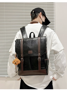 Male model wearing black faux leather backpack with brown trim and puppy pendant charm