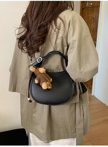 Black lychee leather crescent bag with teddy bear pendant shown on shoulder