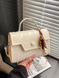 Minimalist beige crossbody bag with woven texture and decorative beaded keychain
