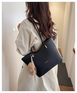 Detail of large black litchi pattern leather tote bag with brown bear charm on model