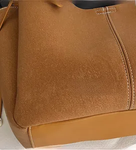 Detail of brown tote bag featuring textured fabric and leather stitching with white seams