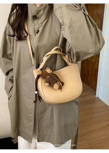 Chic beige bucket bag with teddy bear charm shown on a green trench coat outfit