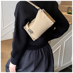 Close-up of beige textured leather handbag with silver studs and metal twist lock