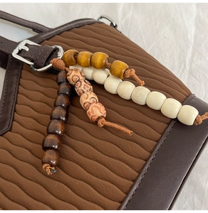 Gros plan du sac seau marron avec plis ondulés et pendentif en perles vintage