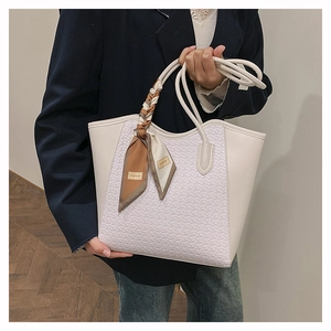 Close-up of white woven tote bag featuring a decorative fashion silk scarf on the handle