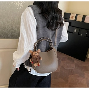Detail of dark brown pebbled leather handbag with cute teddy bear charm and strap