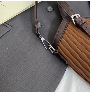 Détail macro du sac à main plissé marron avec bandoulière cuir et boucles argentées