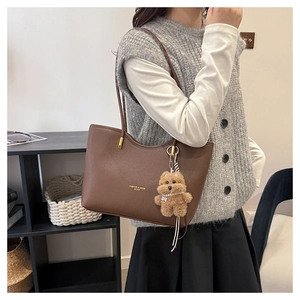 Detail of a brown lychee pattern leather tote bag with gold lettering and a bear charm