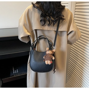 Detail of black pebbled leather bucket bag with cute bear charm on trench coat background