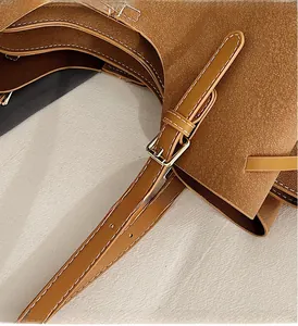 Close-up of golden buckle detail and white stitching on brown leather tote bag strap