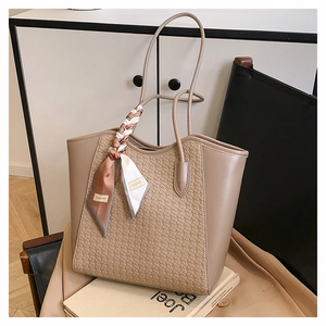 Detail of khaki tote bag with woven texture and fashion scarf handle on a chair