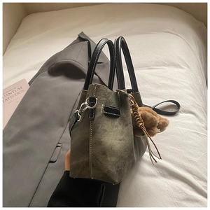 Detail of dark green bucket bag with plush bear charm on white linen background