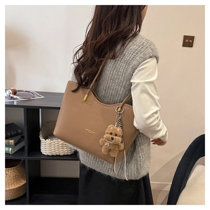 Detail of vintage brown leather tote bag with gold lettering and plush bear charm