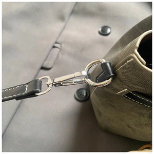 Close-up of silver metal hook and black leather trim on a green bucket bag