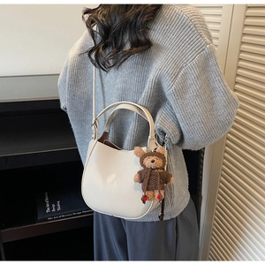 Detail der cremeweißen Hobo-Tasche aus Lychee-Leder mit braunem Strickbären-Anhänger