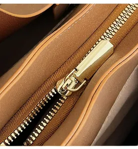 Close-up of smooth gold metal zipper and fine stitching on brown leather tote bag