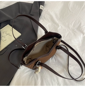 Détail du sac seau marron avec surpiqûres vagues et charm perlé sur lit blanc