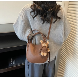 Detail der braunen Leder-Handtasche mit Litschi-Muster und Teddy-Anhänger am Modell