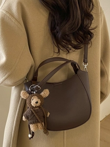 Dark brown lychee texture bucket bag with bear charm on model in autumn coat