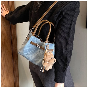 Detail of denim tote bag with leather trim, metal twist lock and plush bear charm