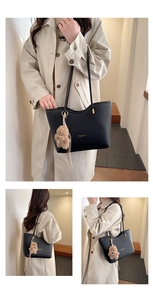 Detail of a black pebbled leather tote bag with a brown plush dog charm and gold hardware